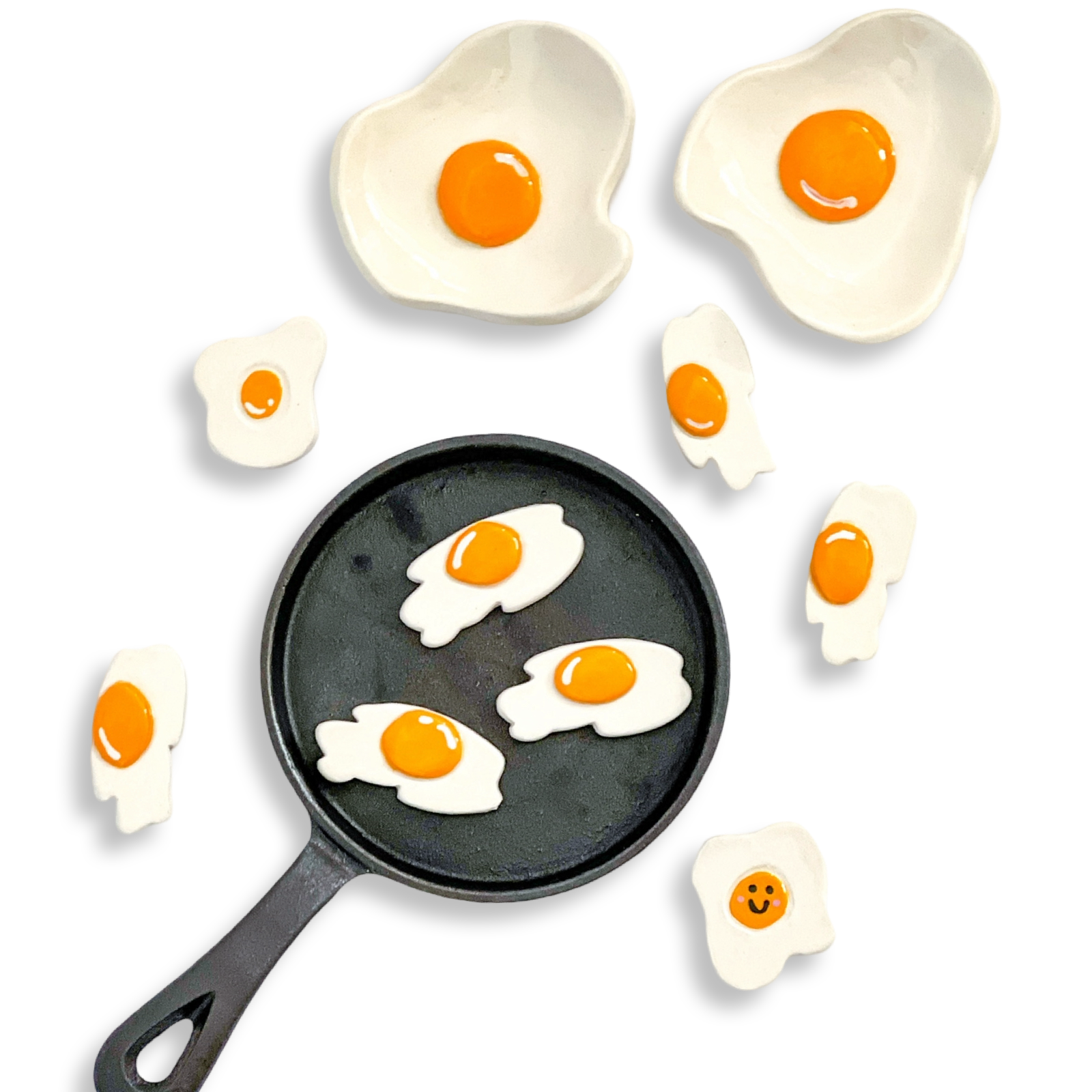 Black frying pan with ceramic egg dishes around it on a white background