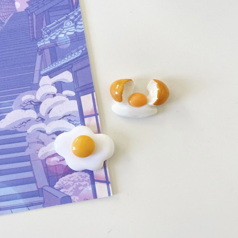 Set of two magnets, one fried egg and one raw egg freshly cracked with shells on side.