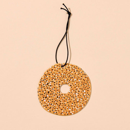 Everything bagel air freshener on a black string on a beige background