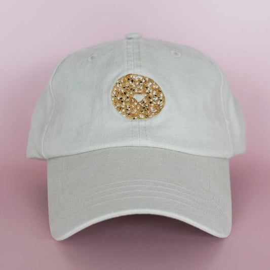 Khaki colored cap with a embroidered everything bagel design on front, pictured here on a pink background