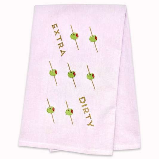 White kitchen towel with skewered olives design and text "extra dirty" on a white background