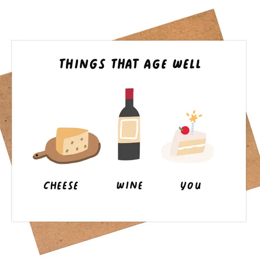 Greeting card with text "Things that age well... Cheese Wine You" and illustration of a cheese wedge on wood paddle, bottle of wine, and slice of birthday cake with a single cherry and candle on top.