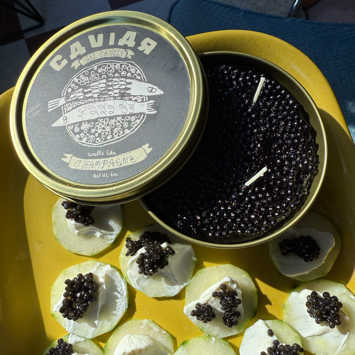 Caviar candle in a gold container with black caviar on top of creme fraiche on a yellow plate.