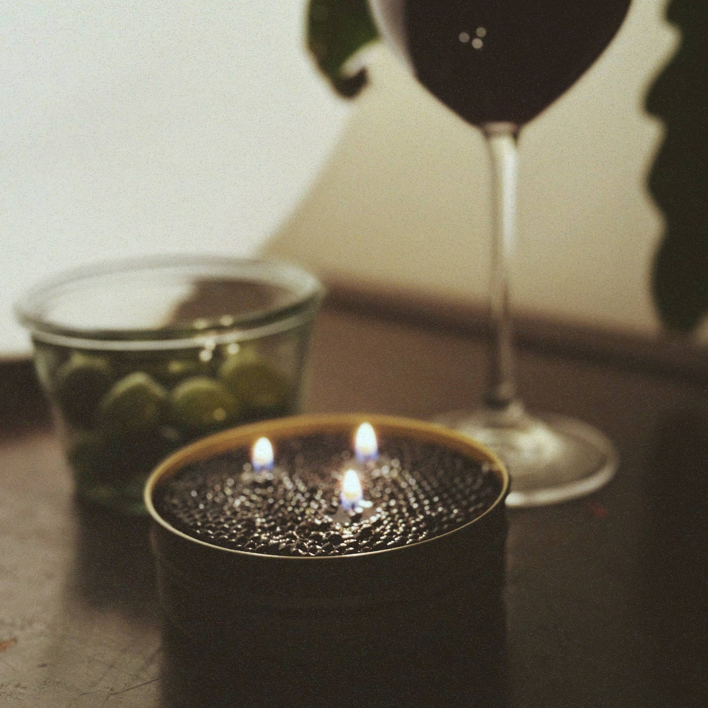 Caviar candle in a black holder with a glass of red wine and a bowl of olives on a table.