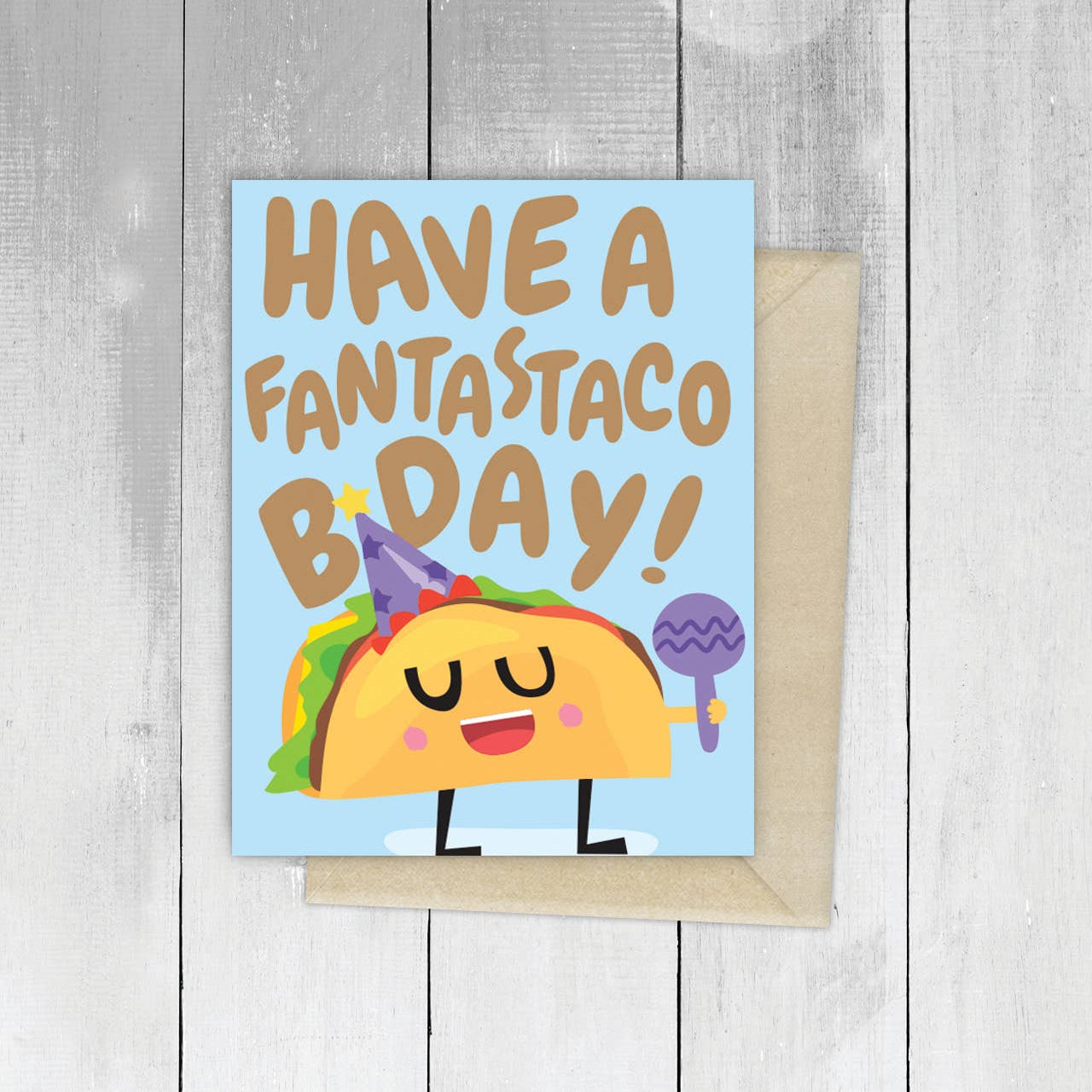 Birthday card with a cartoon taco and text 'Have a fantastaco bday!' on a wooden surface.
