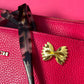  handbag with a gold bowtie pasta pin detail on a pink background