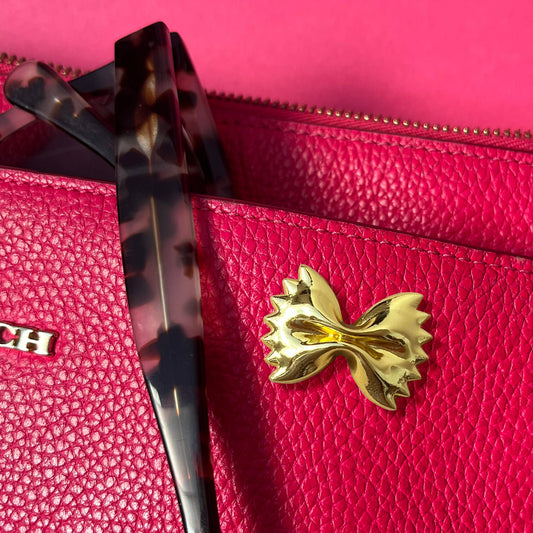  handbag with a gold bowtie pasta pin detail on a pink background