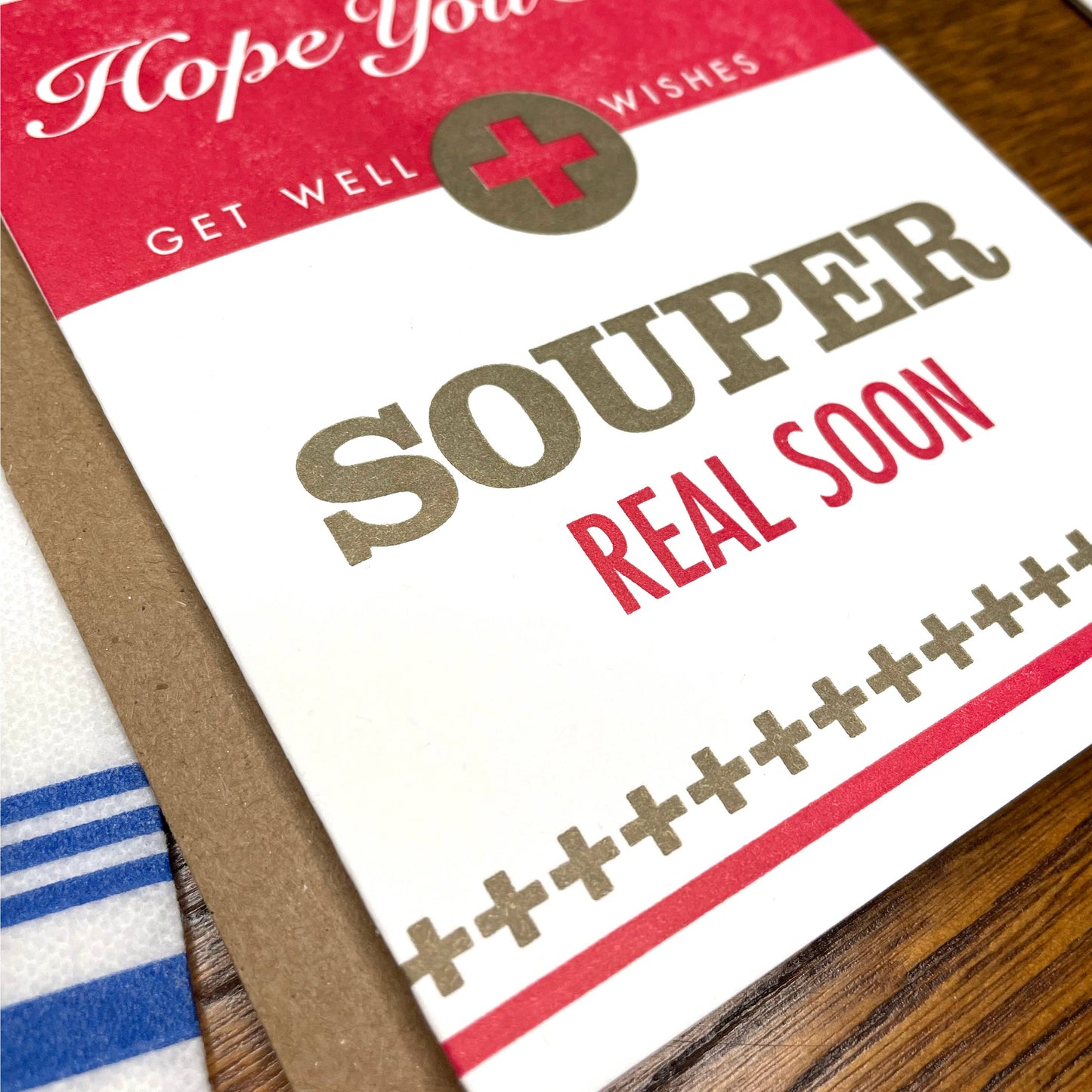 Get well card with 'Hope you feel Souper Real Soon' text on a wooden surface
