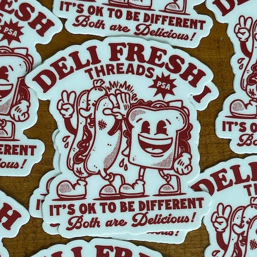 Stickers with 'Deli Fresh Threads' and 'It's Ok to be Different, Both are Delicious!' text on a wooden surface.