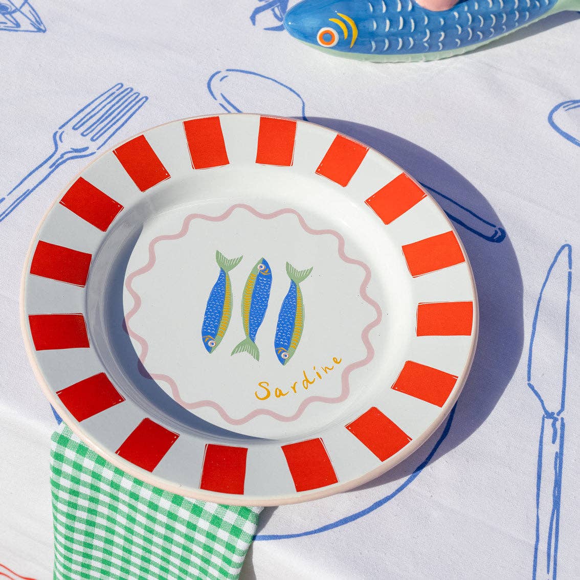 Decorative plate with red stripes and fish illustration on a tablecloth with cutlery drawings