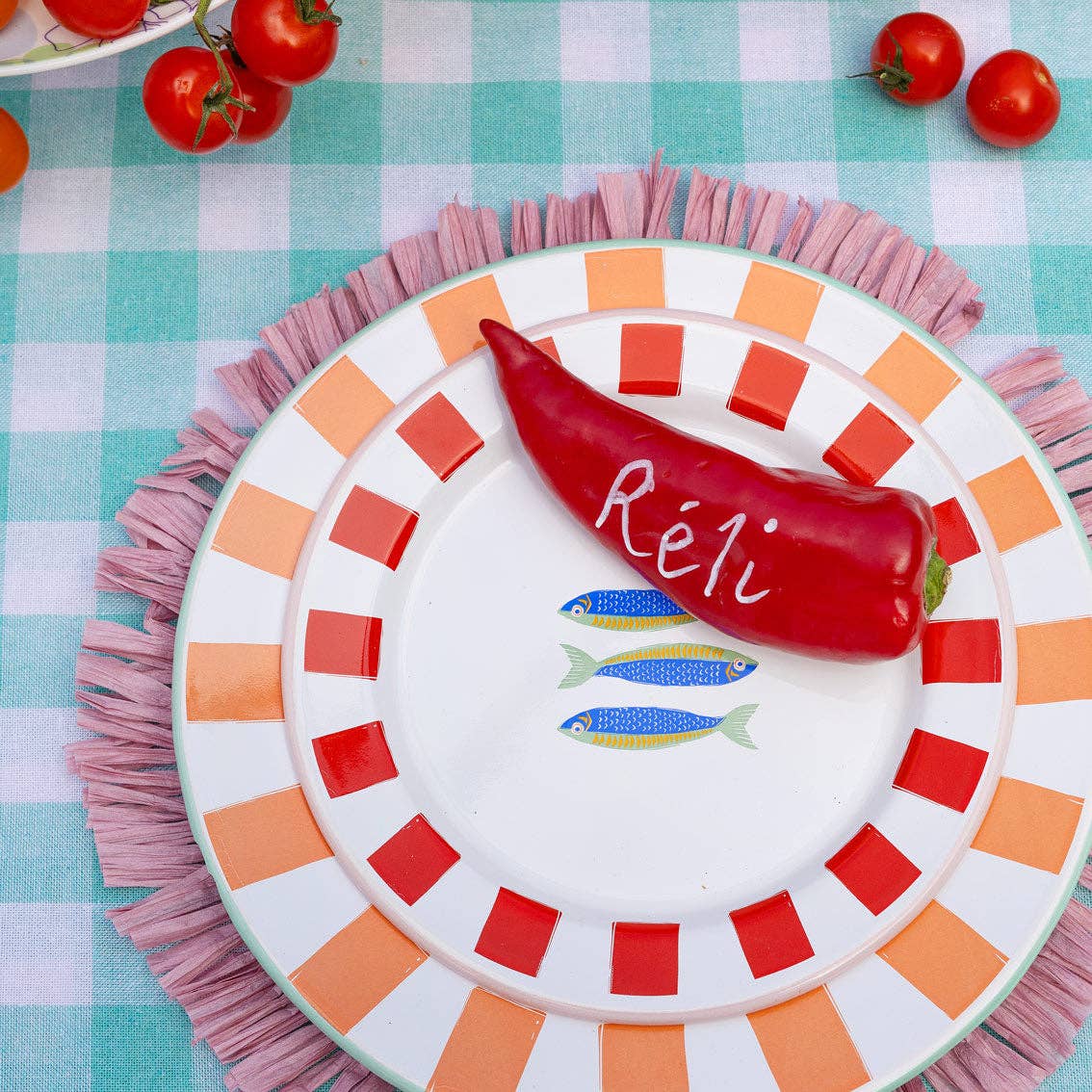 Decorative plate with a red pepper and the name 'Reli' on a checkered tablecloth.