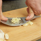Person using the fish-shaped garlic press on a wooden cutting board with minced garlic.