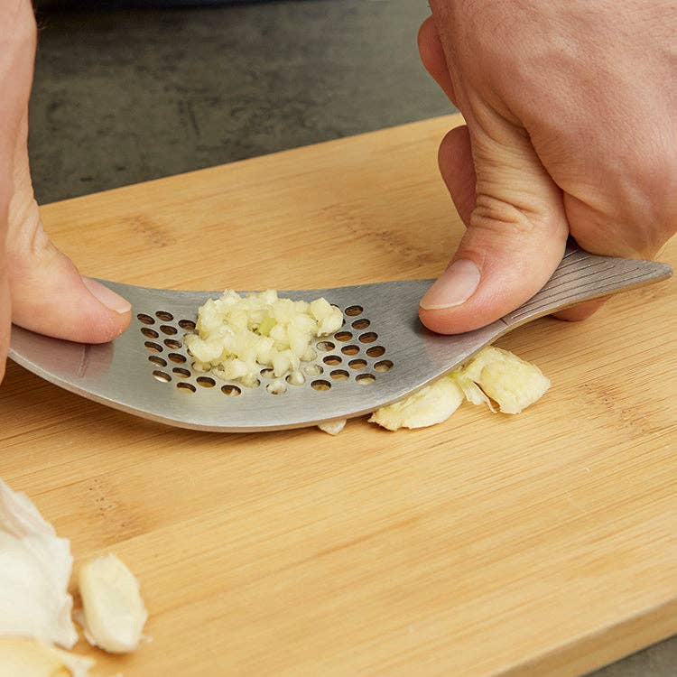 Person using the fish-shaped garlic press on a wooden cutting board with minced garlic.