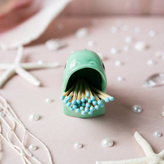 Green ceramic matchbox with matches on a decorative surface with starfish and pearls