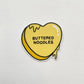 Heart-shaped sticker with 'Buttered Noodles' text on a light gray background
