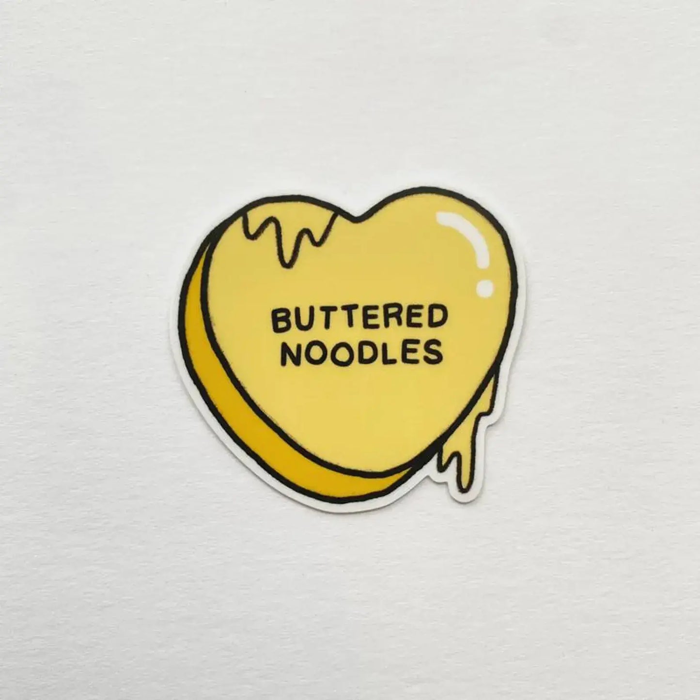 Heart-shaped sticker with 'Buttered Noodles' text on a light gray background