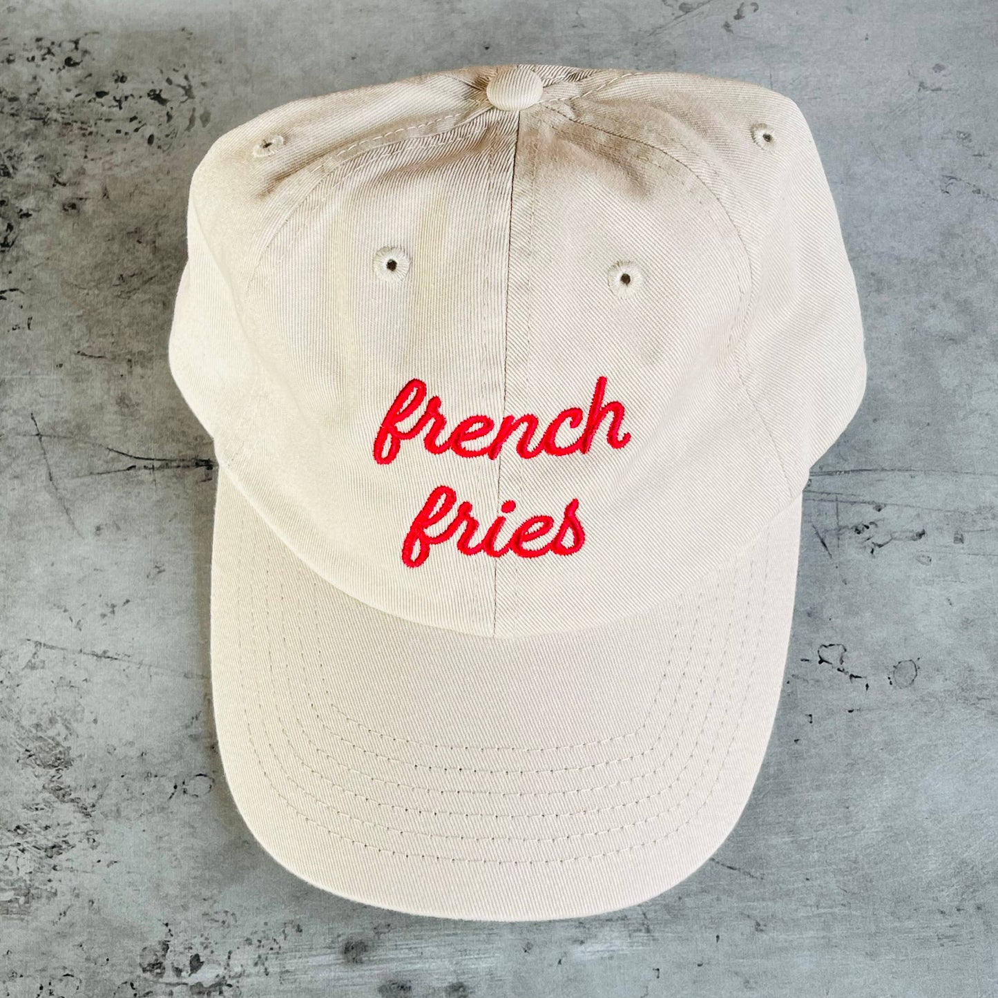 Beige cap with 'french fries' in red text on a concrete surface