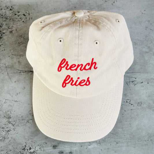 Beige cap with 'french fries' in red text on a concrete surface
