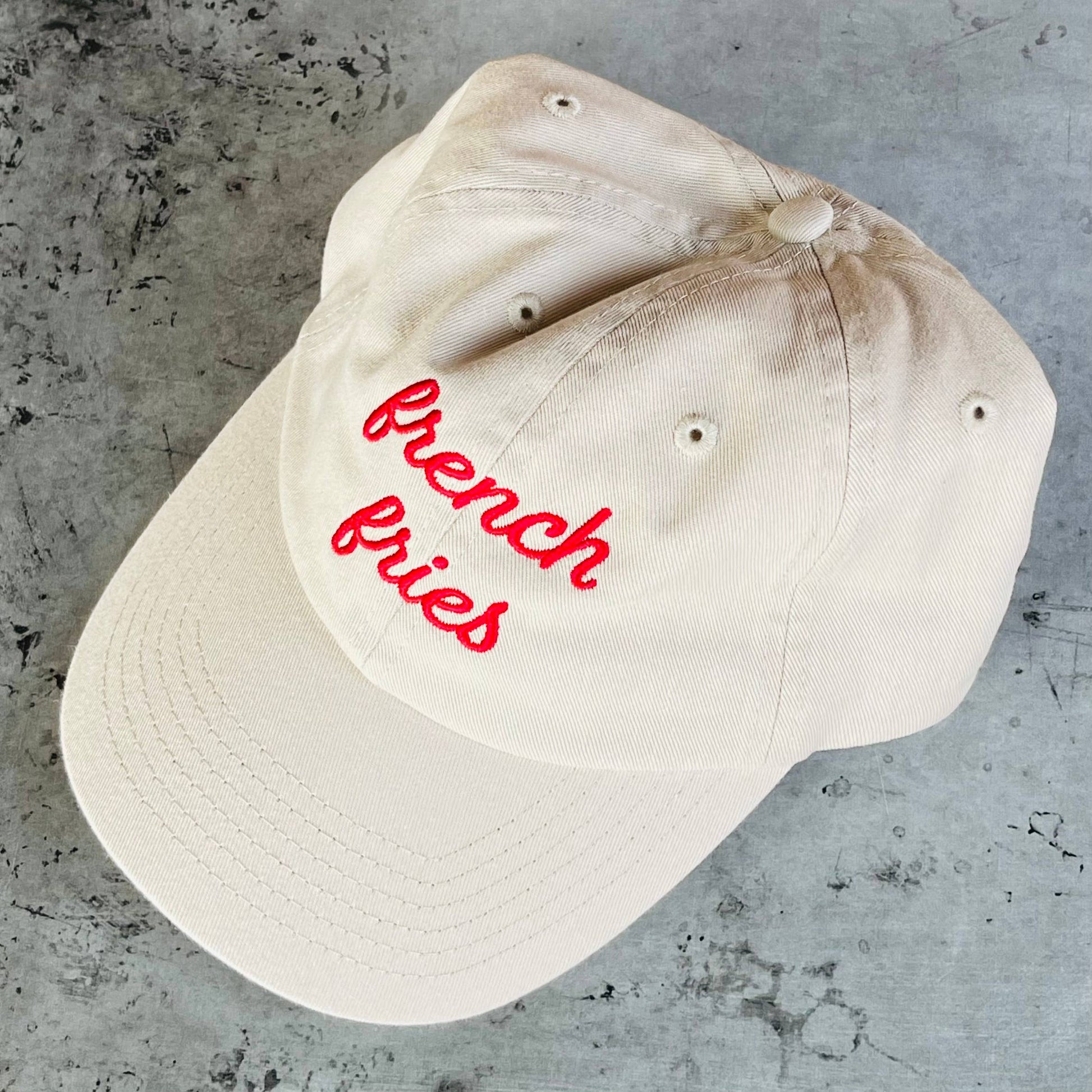 Beige cap with 'french fries' in red text on a gray surface