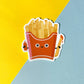 Cartoon-style French fries in a red box with a face, holding a ketchup squeeze bottle and ketchup dipped fry, on a yellow and blue background