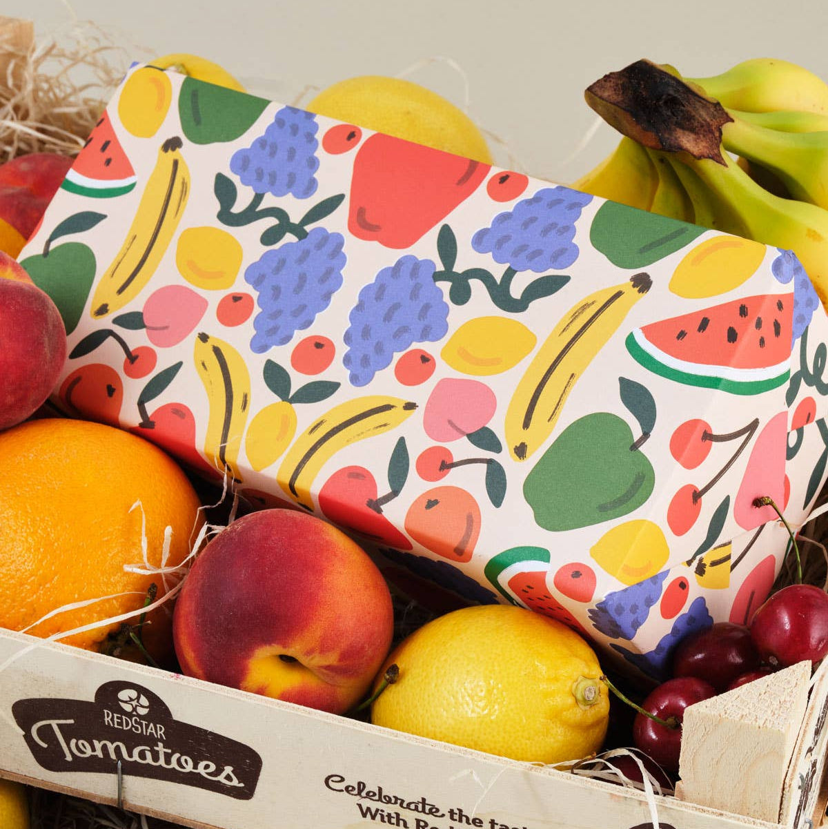 box covered with the sheet of gift wrap with various fruits on it including bananas, apples, grapes, watermelon, cherries, oranges, lemons and peaches 