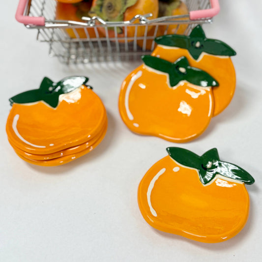 Stack of persimmon trinket dishes with green leaves on a white background