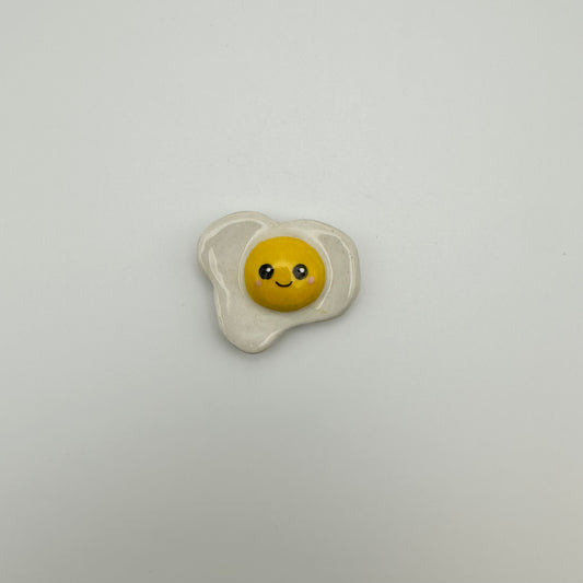 small ceramic fried egg magnet with a smiley face painted on 