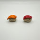 Two small ceramic magnets resembling sushi with smiling faces on a white background