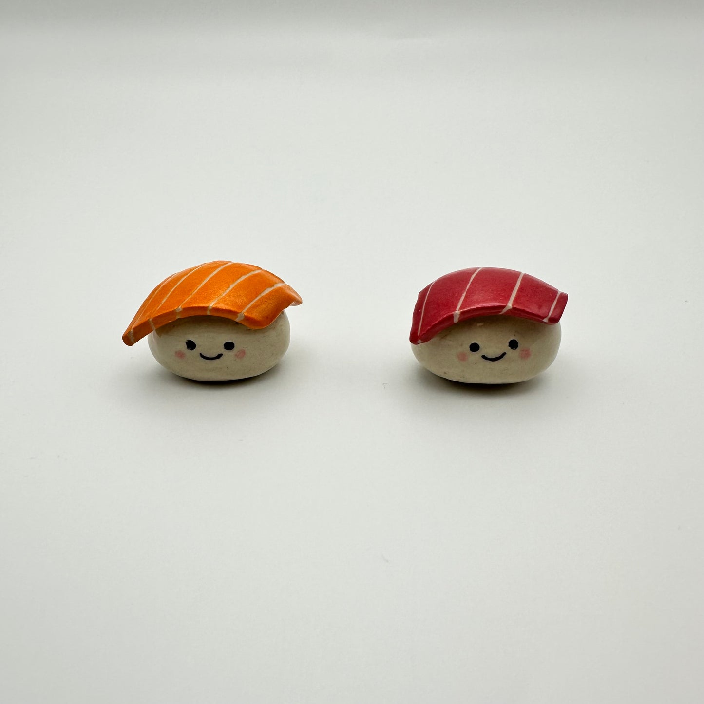 Two small ceramic magnets resembling sushi with smiling faces on a white background