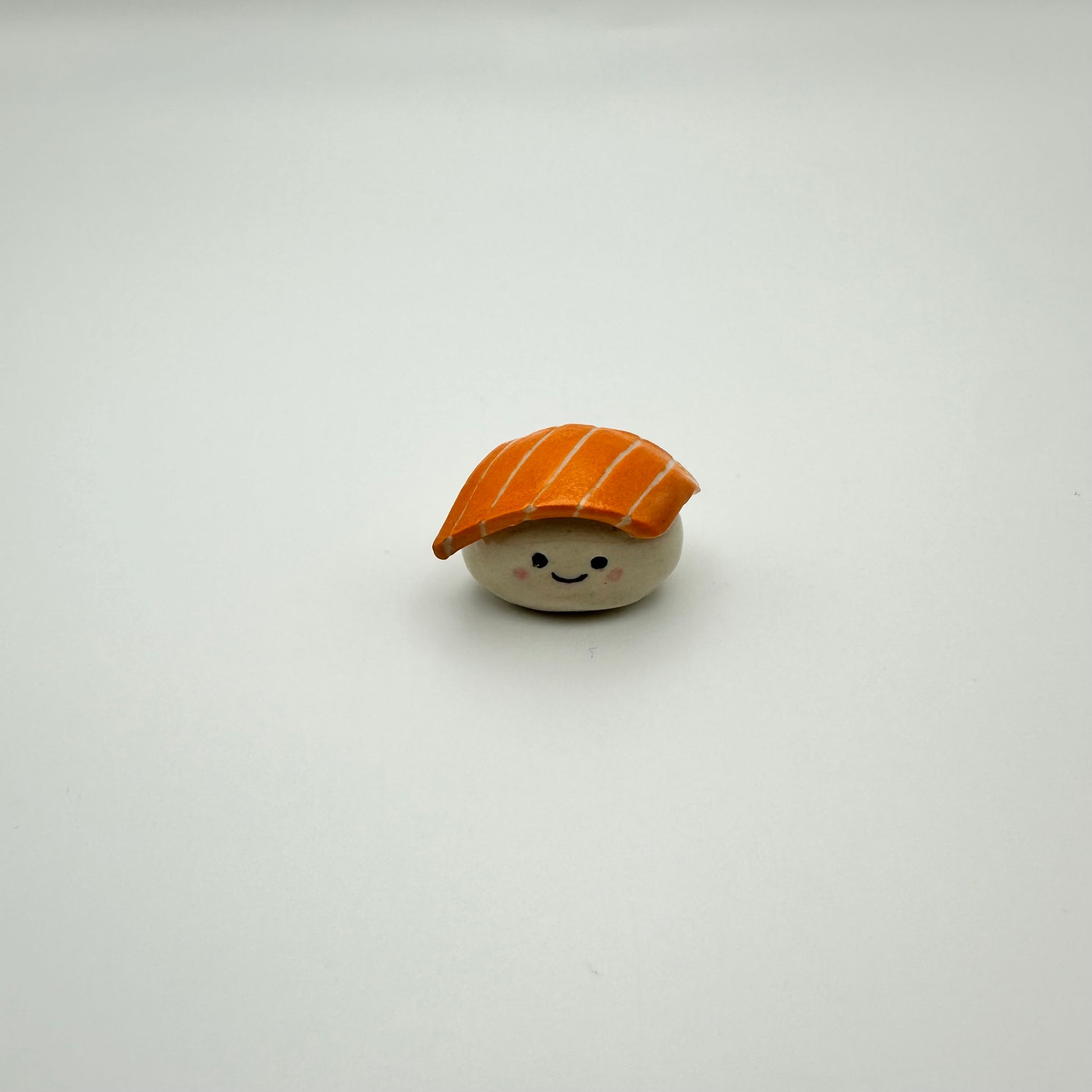 Small toy resembling a piece of sushi with a smiling face on a white background