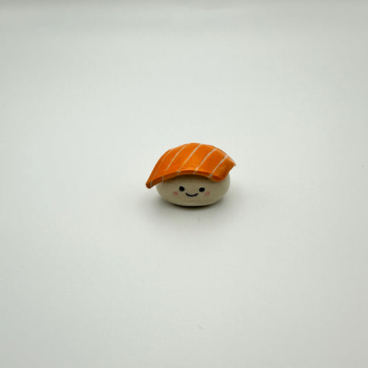 Small toy resembling a piece of sushi with a smiling face on a white background