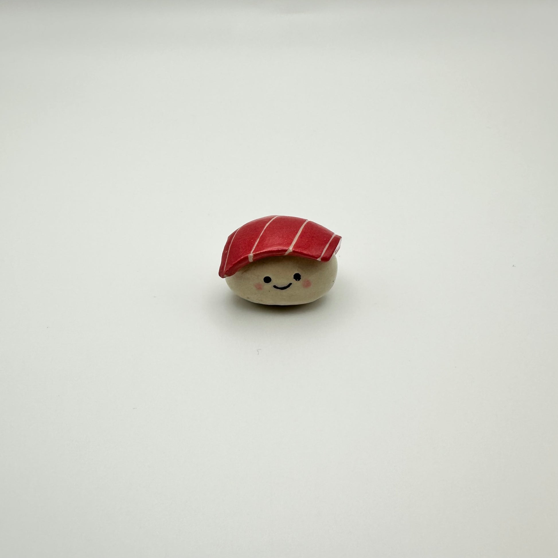Small ceramic sushi magnet resembling a piece of tuna nigiri sushi with a smiley face on a white background