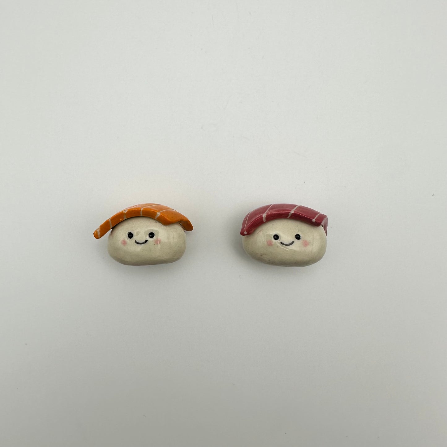 Two small ceramic sushi magnets, one salmon one tuna, with smiling faces on a light gray background
