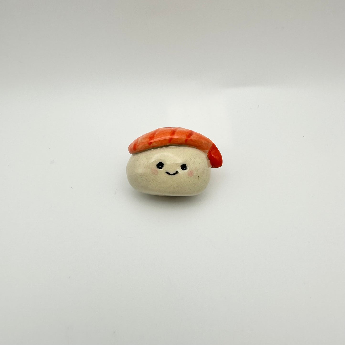 Small ceramic made to look like a shrimp nigiri sushi with a face on a white background