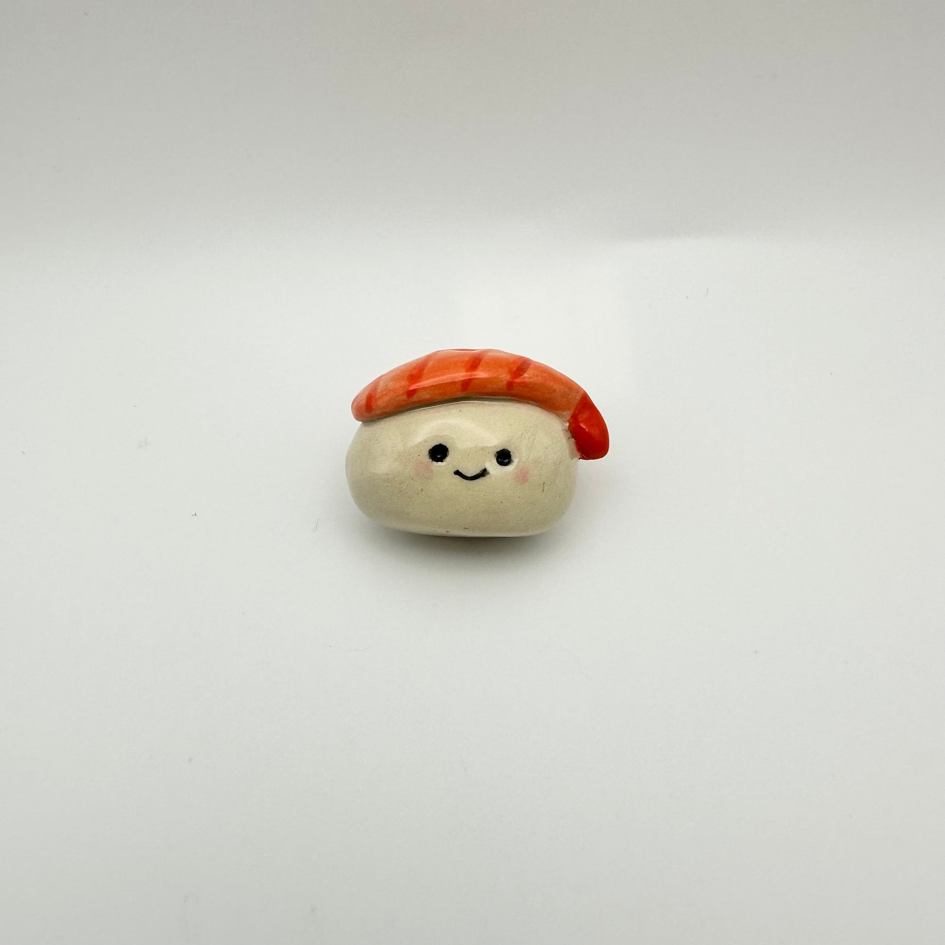 Small ceramic made to look like a shrimp nigiri sushi with a face on a white background
