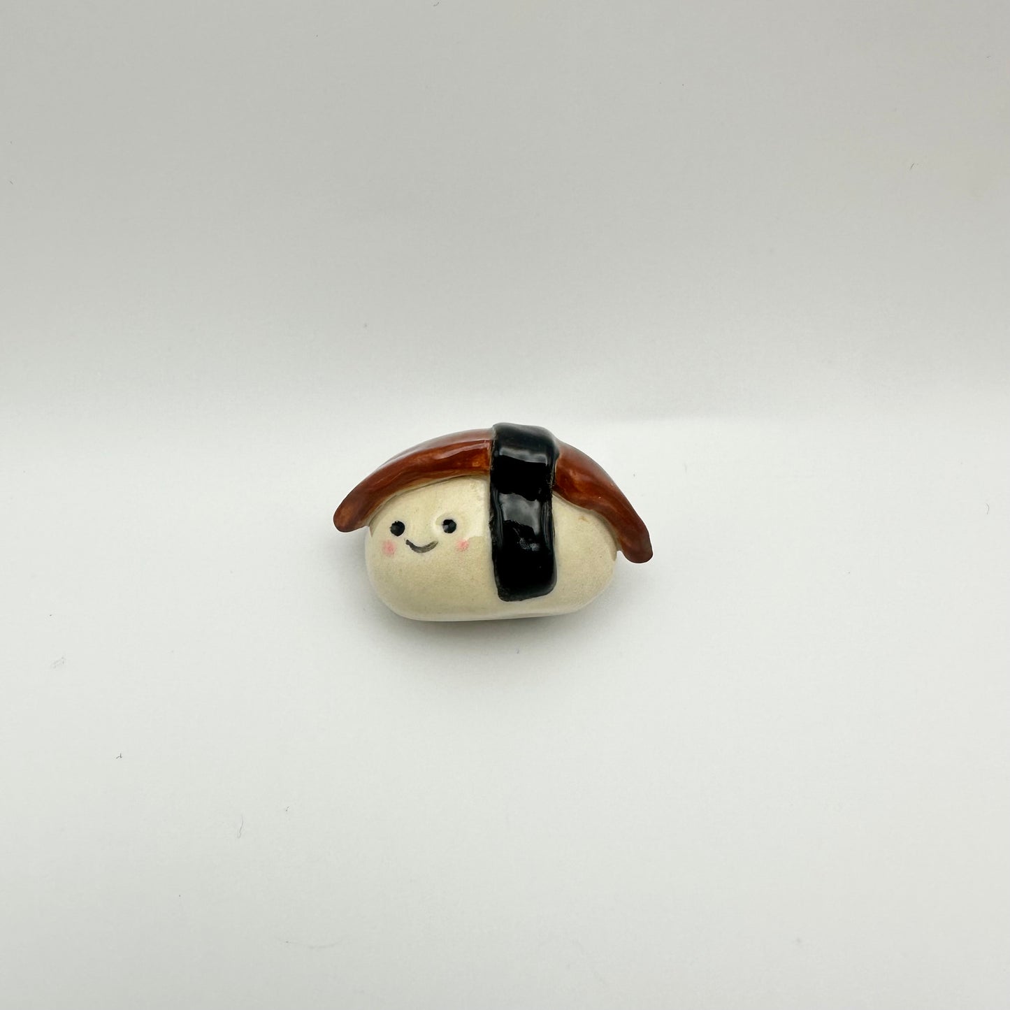 Small ceramic unagi/eel sushi figurine on a white background