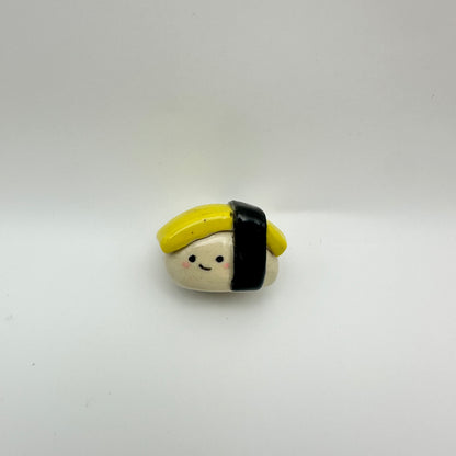 Tamago/egg sushi-shaped ceramic figurine with a face on a white background
