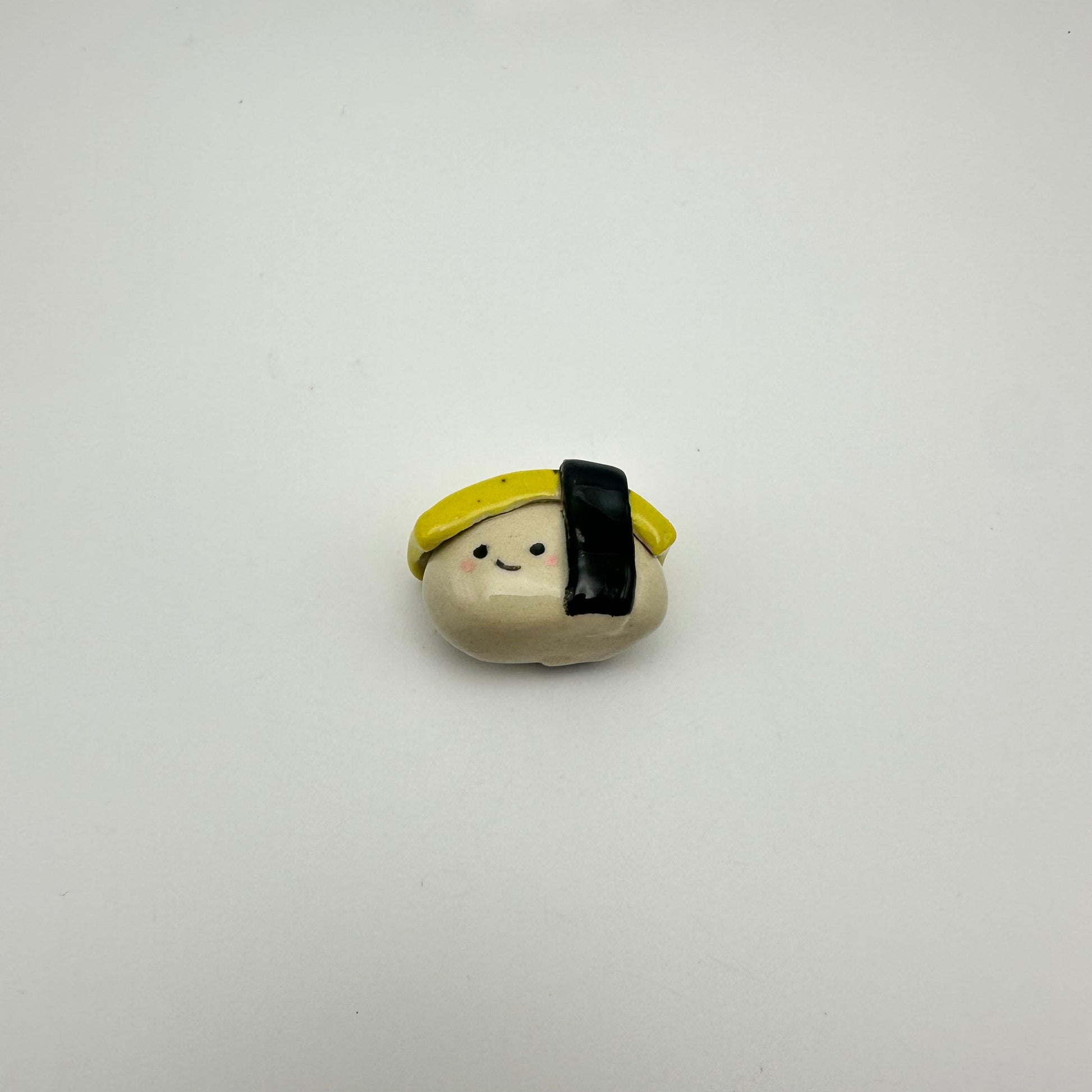 Small ceramic figurine resembling a piece of tamago/egg sushi on a white background