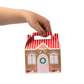 Hand holding a gingerbread house-themed gift box with red and white striped handle on a white background