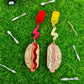 Hot dog earrings with ketchup and mustard details on them. Earrings are pictured on grass with a toy wagon and utensils.