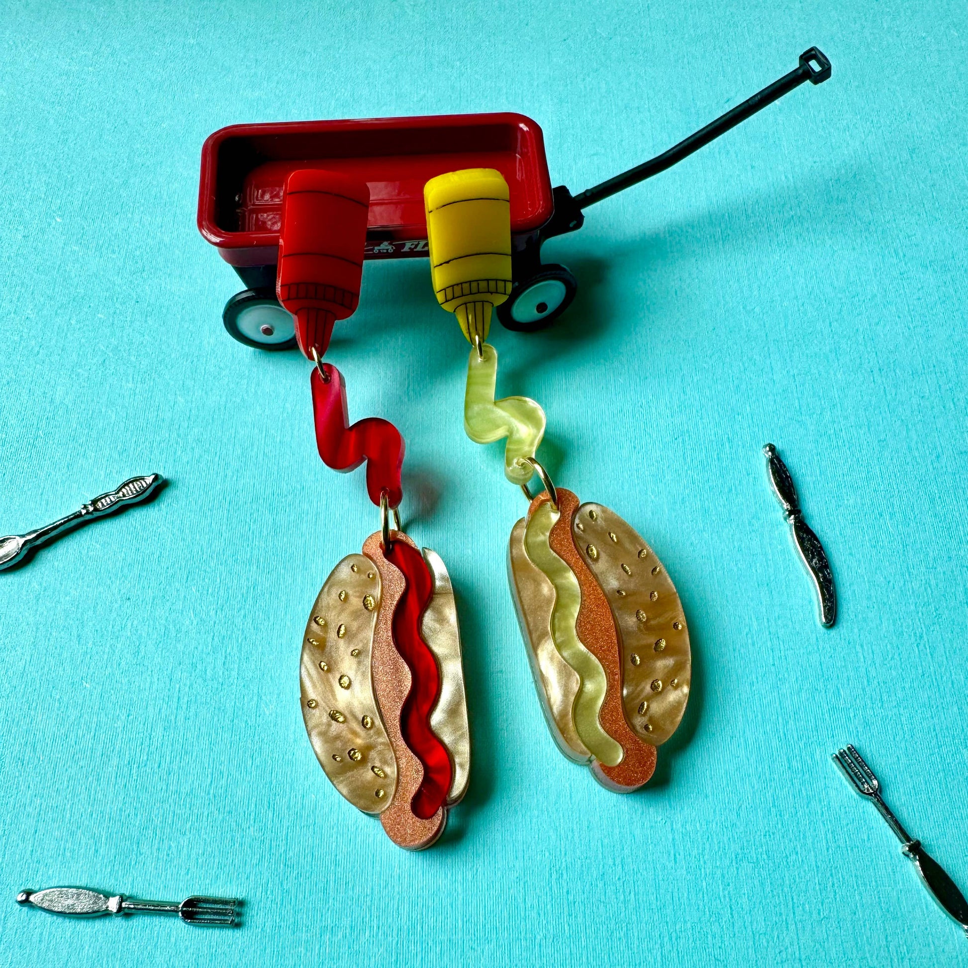 Earrings resembling hot dogs with buns with ketchup and mustard details on a blue background
