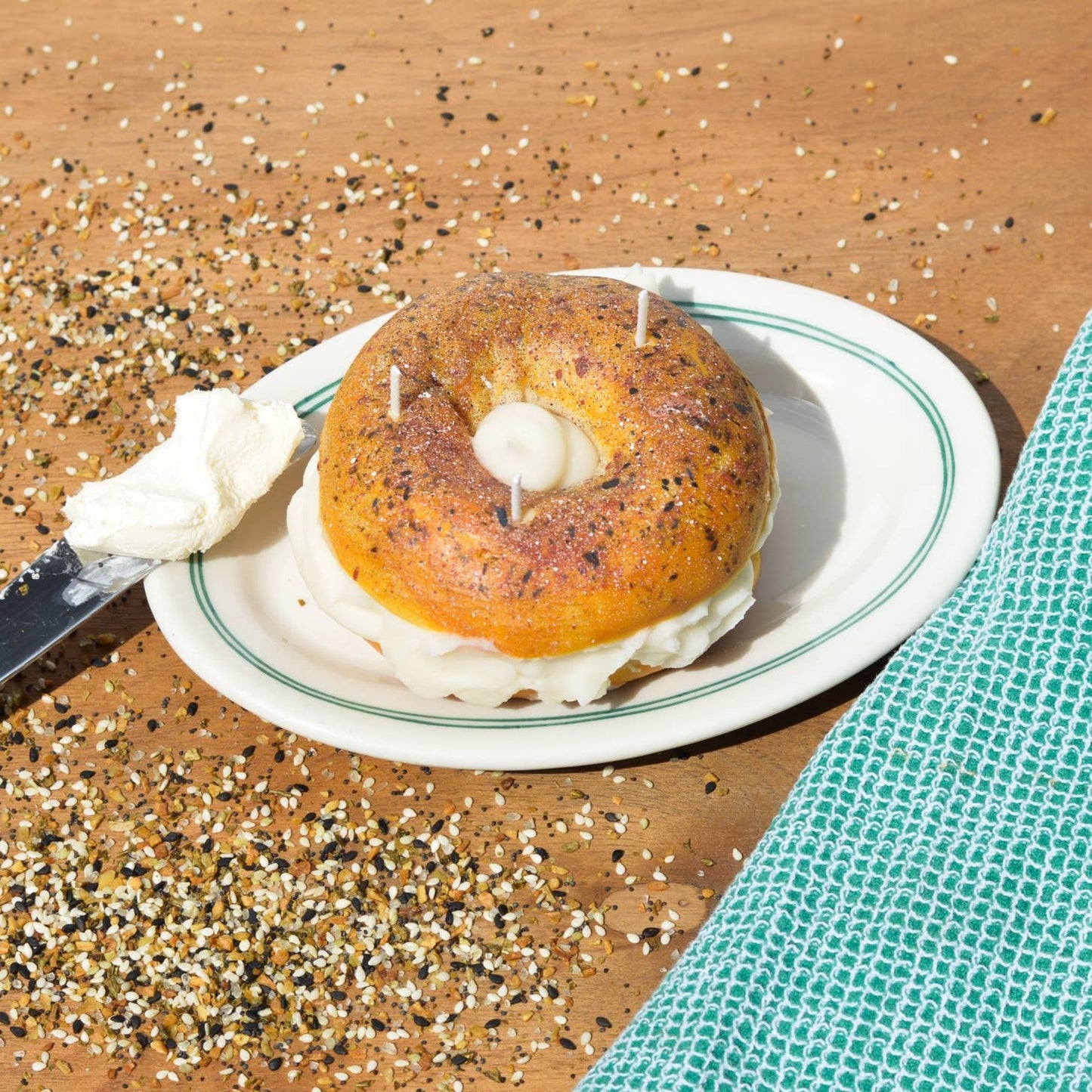 Everything bagel candle shown on a plate with a knife full of cream cheese.