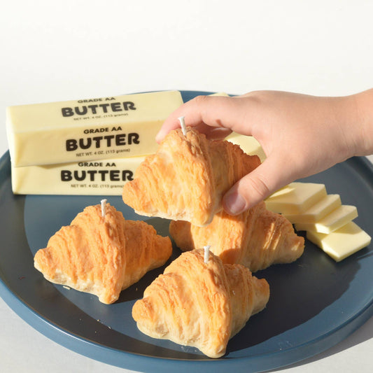 Hand reaching for a pile of four croissant candles on a plate next to slabs of butter.