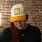 Person wearing a cap with a banana graphic patch against a brick wall