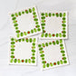 Four square cloth cocktail napkins with green stuffed olive design on a white background