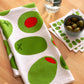Olive-themed kitchen towel and coasters on a wooden surface with a bowl of olives.