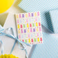 Greeting card with colorful gummy bear pattern on a white surface with blue ribbons and yellow balloons.