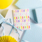 Greeting card with colorful gummy bear pattern surrounded by blue and white striped gift boxes on a white background.