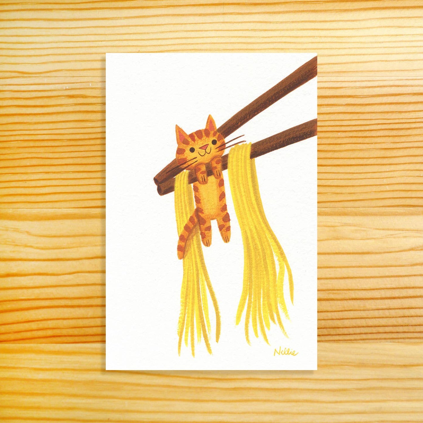 A vertical art print featuring a cute illustration of an orange tabby cat hanging from brown chopsticks with yellow noodles, displayed on a light wood grain background.