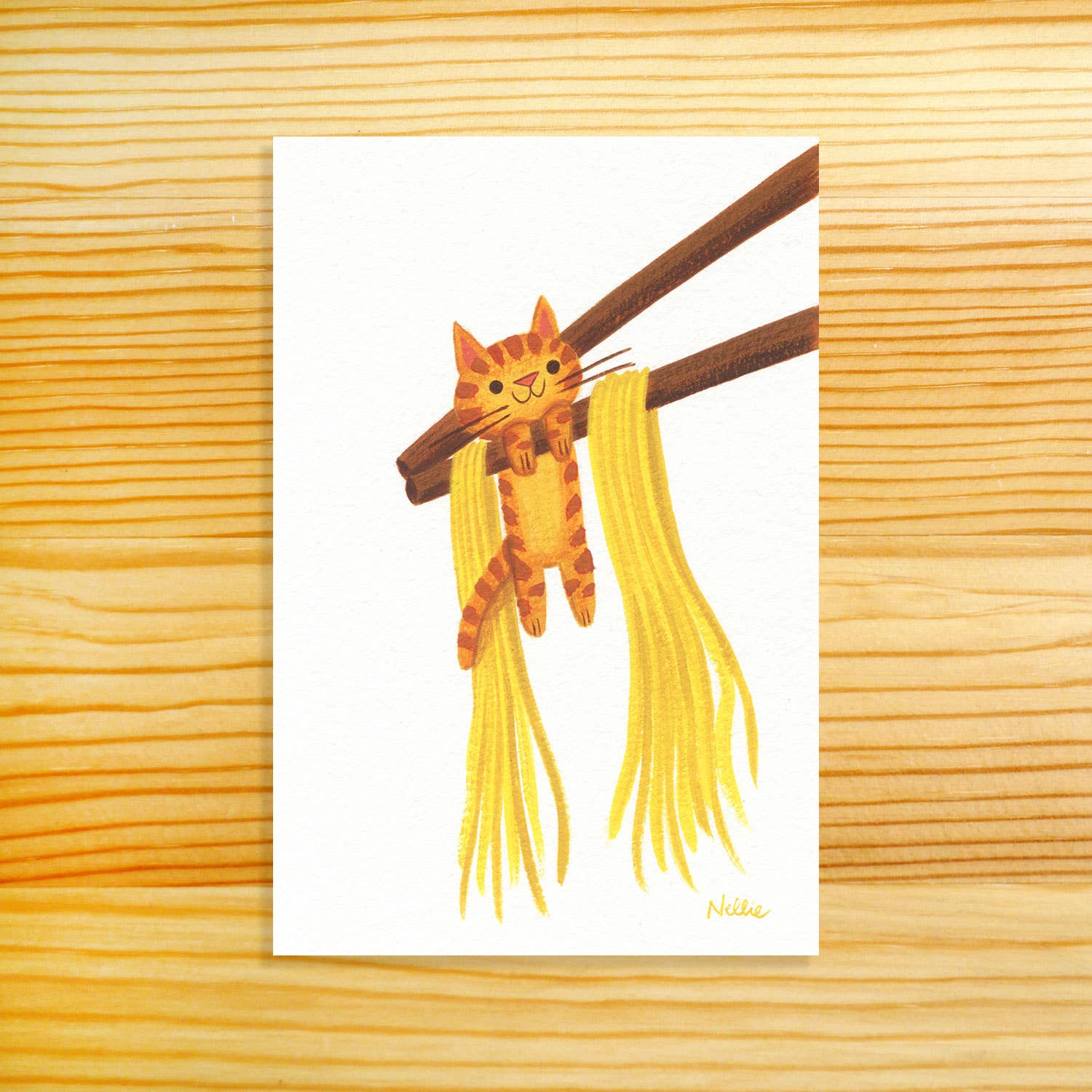 A vertical art print featuring a cute illustration of an orange tabby cat hanging from brown chopsticks with yellow noodles, displayed on a light wood grain background.